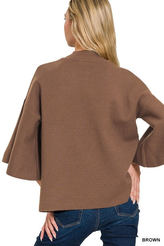 Woman wearing a brown bell sleeve sweater top with blue denim jeans with a white background