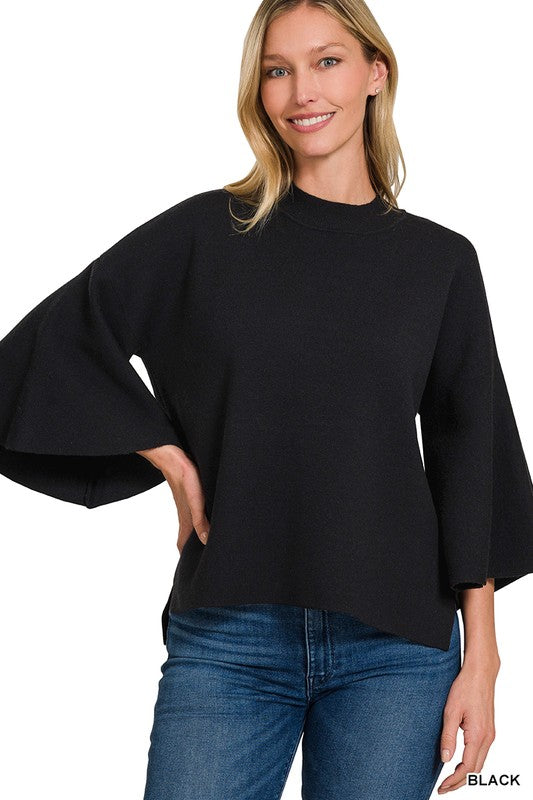 Woman wearing a black bell sleeve sweater top with blue denim jeans with a white background