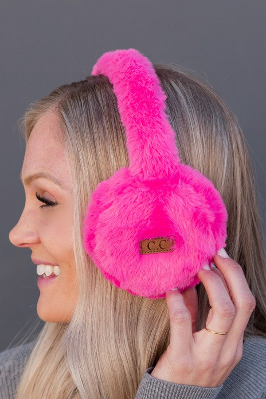Person wearing bright pink furry earmuffs with a brand logo against a gray background