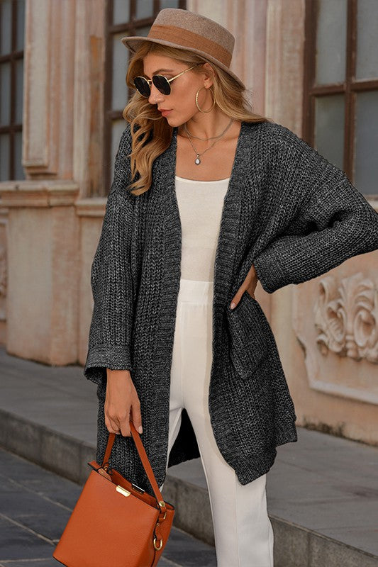Woman wearing a gray cardigan, white pants, and a brown hat outdoors.