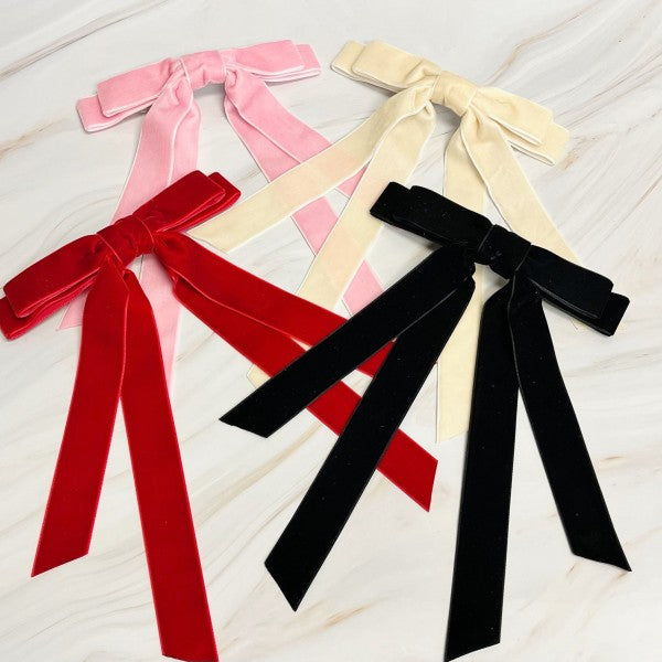 Four velvet ribbons in red, pink, beige, and black on a light wooden surface.