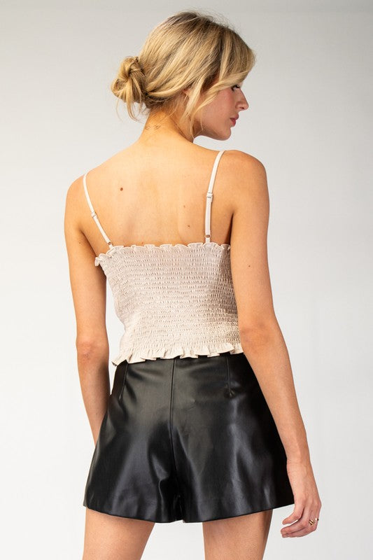 Woman wearing a white lace top and black leather shorts on a plain background