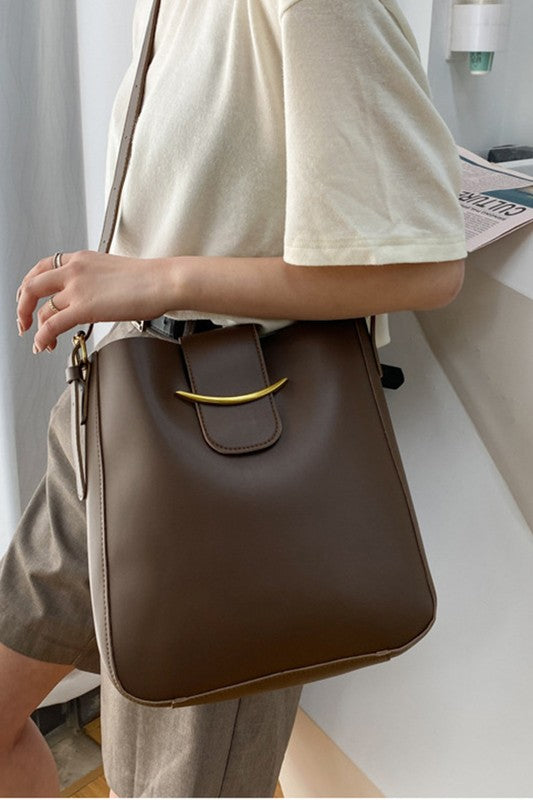 Person holding a brown leather bag with a gold buckle.