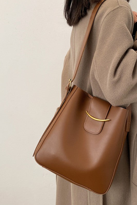 Brown leather handbag held by a person wearing a beige coat against a neutral background