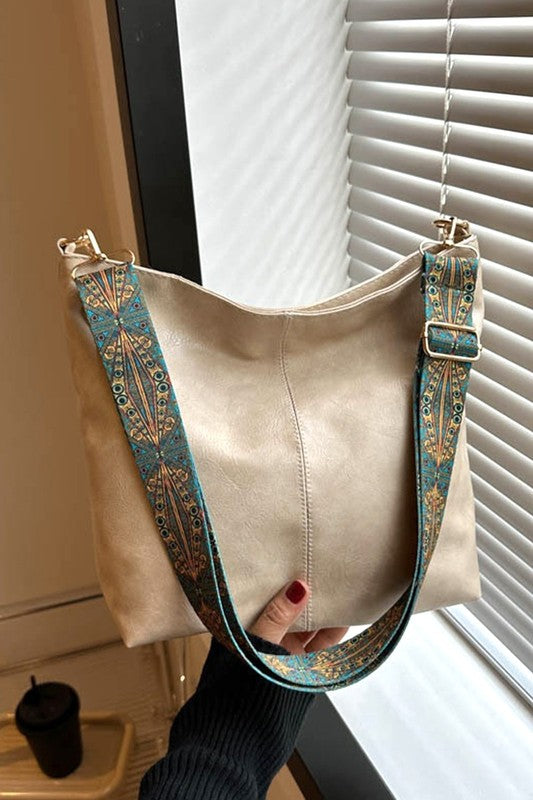 Beige handbag with decorative straps held by a person in front of a window.