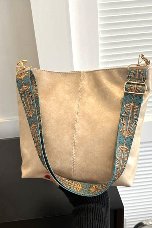 Beige handbag with decorative strap on a stand against a neutral background