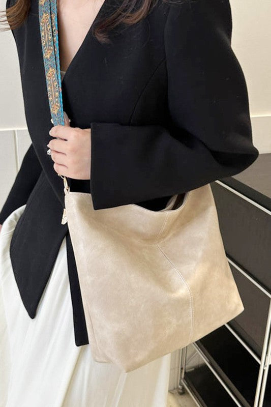 Person holding a beige tote bag with a decorative strap in an indoor setting
