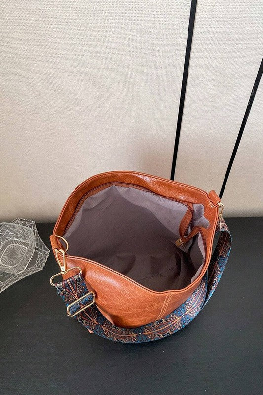 Brown leather handbag with floral patterned strap on a dark surface