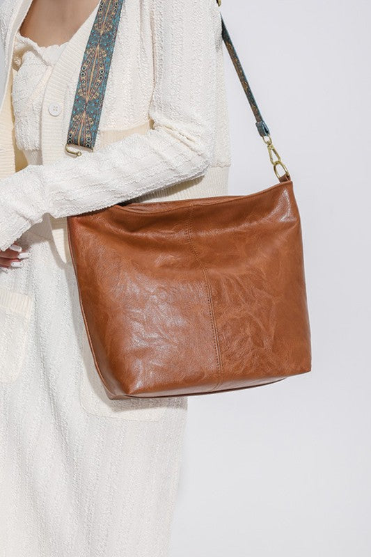 Brown leather handbag held by a person wearing a white outfit on a light background
