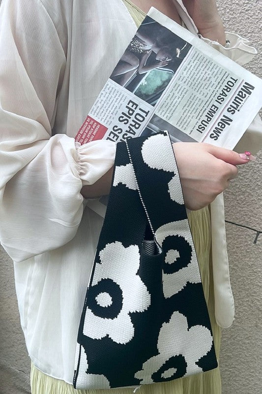 Person holding a black and white patterned bag with a newspaper.