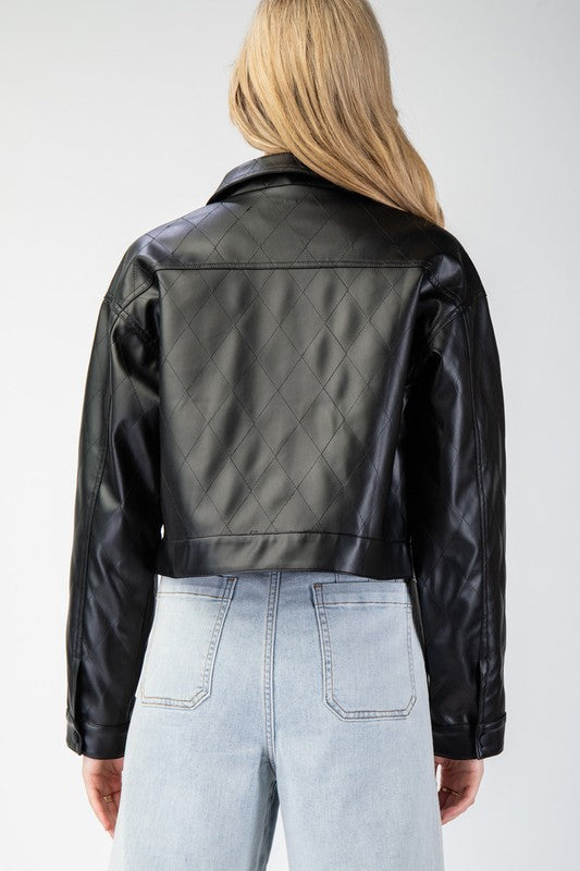 Person wearing a black quilted leather jacket and light blue jeans on a white background