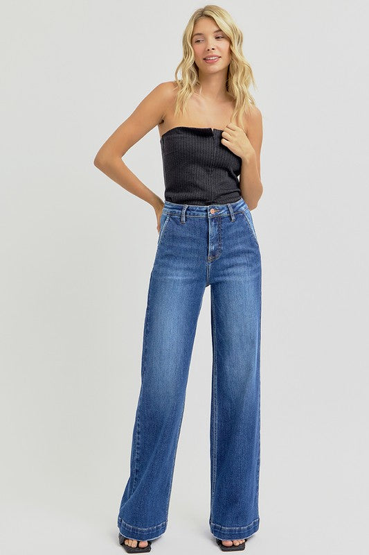 Woman wearing a black strapless top and blue jeans on a light gray background