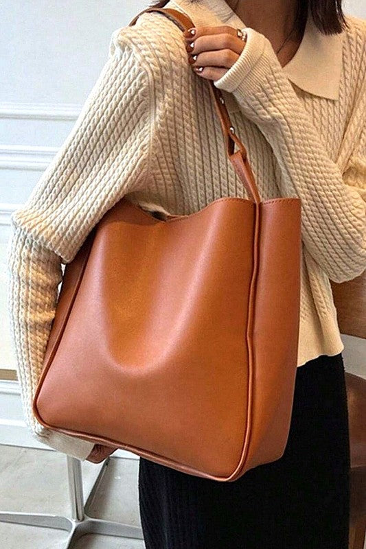 Person holding a brown leather handbag wearing a beige sweater.