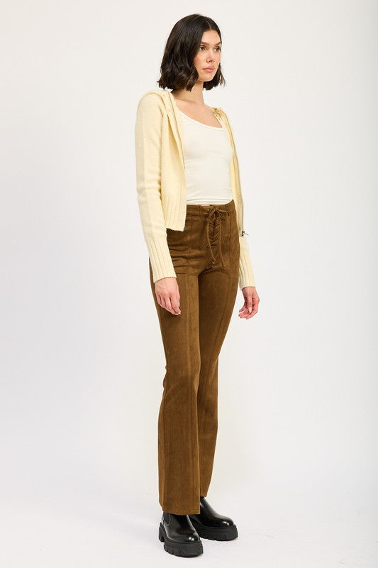 Woman wearing a beige cardigan, white top, and brown corduroy pants on a white background