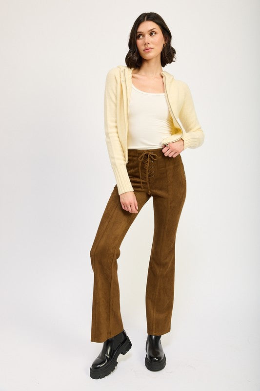Woman wearing a cream cardigan, white top, and brown pants on a white background