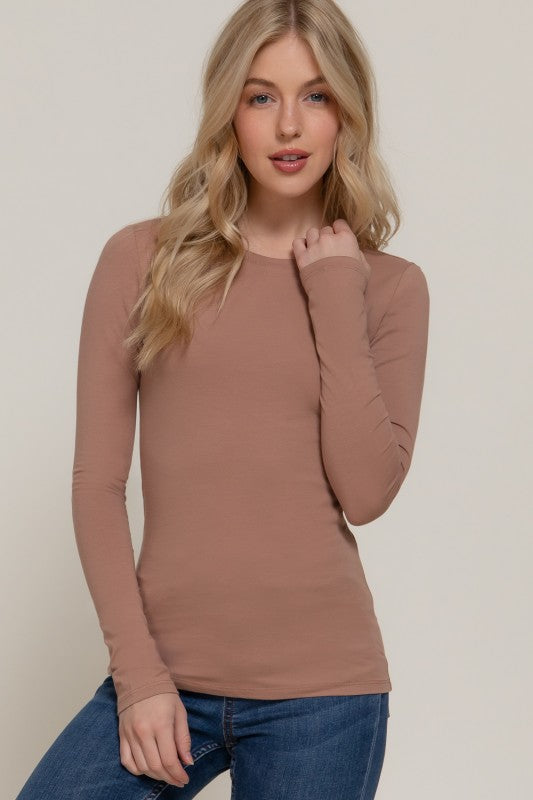 Woman wearing a brown long-sleeve top and blue jeans against a beige background