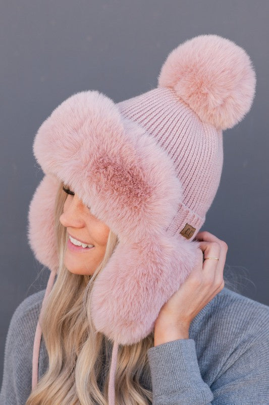 Person wearing a pink knit hat with two large pom-poms against a gray background
