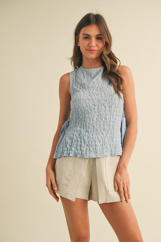 Woman wearing a light blue sleeveless top and beige shorts on a beige background