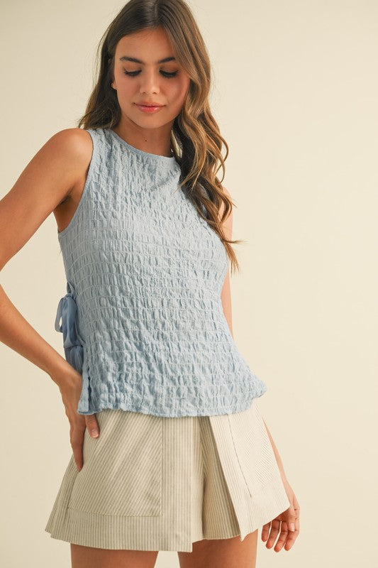 Woman wearing a light blue sleeveless top and beige skirt on a beige background