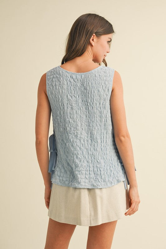 Woman wearing a light blue textured sleeveless top and beige skirt on a beige background