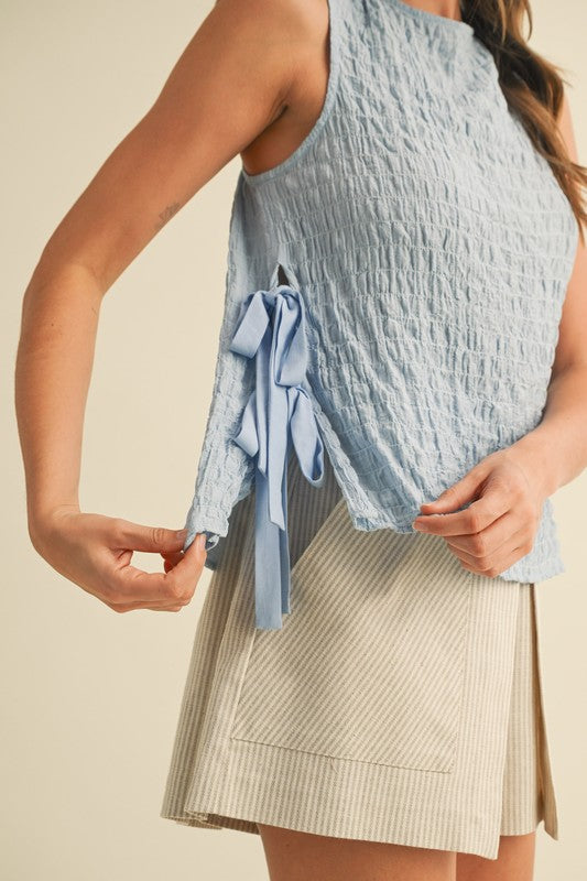 Light blue sleeveless top with a tie detail worn by a person on a beige background
