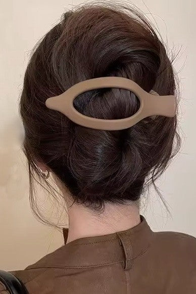 Person with a beige hair clip in their dark hair against a neutral background