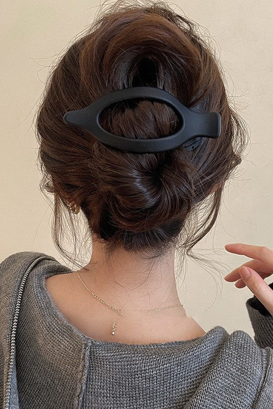 Person with a stylish hair bun held by a black hair clip against a neutral background