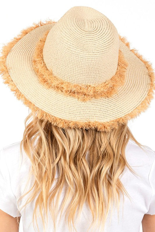 Beige straw hat with frayed edge worn by a person with long blonde hair on a white background