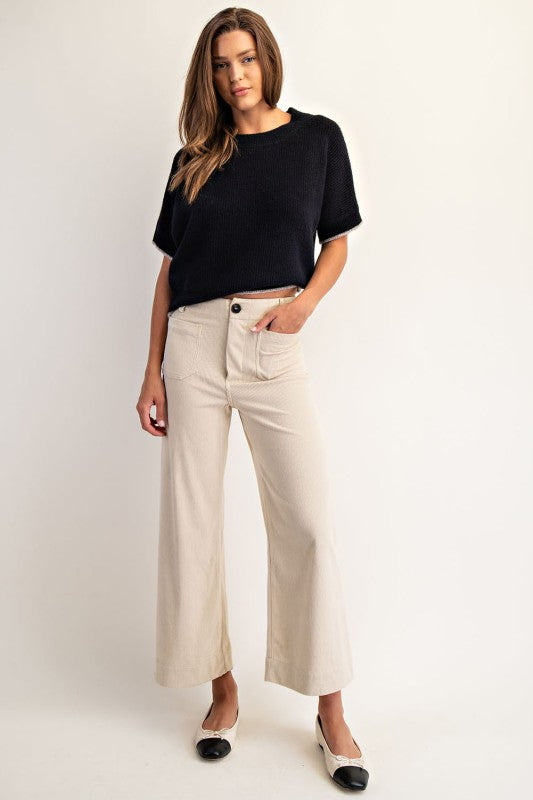 Woman wearing a black top and beige pants on a white background