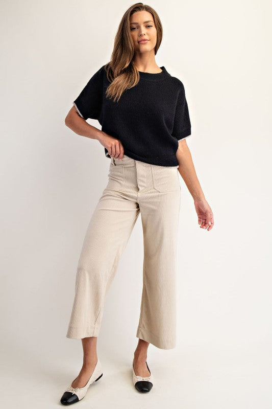 Woman wearing a black top and beige pants on a white background