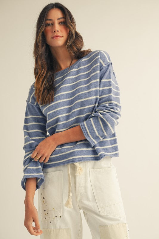Woman wearing a blue and white striped sweater with white pants on a plain background