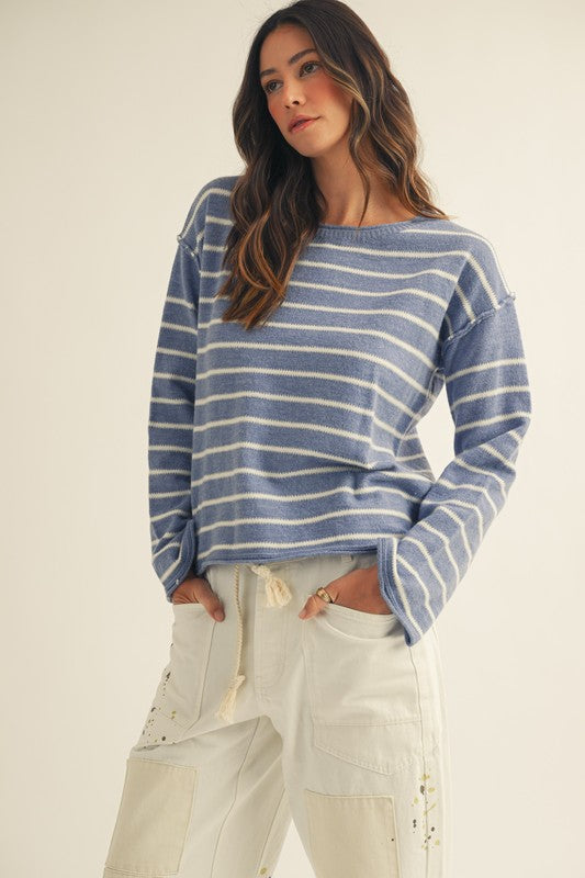 Woman wearing a blue and white striped sweater with beige pants on a plain background