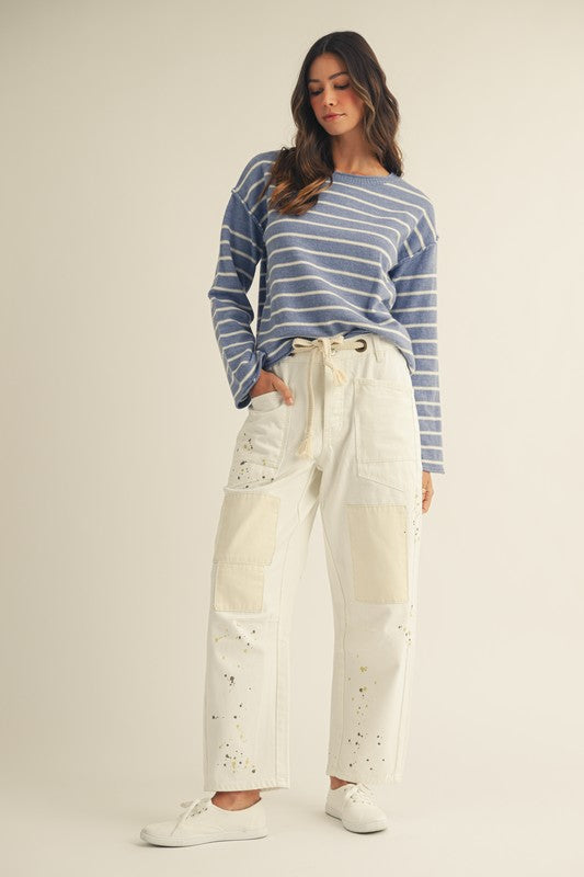 Woman wearing a blue and white striped sweater and white pants with star patterns on a beige background