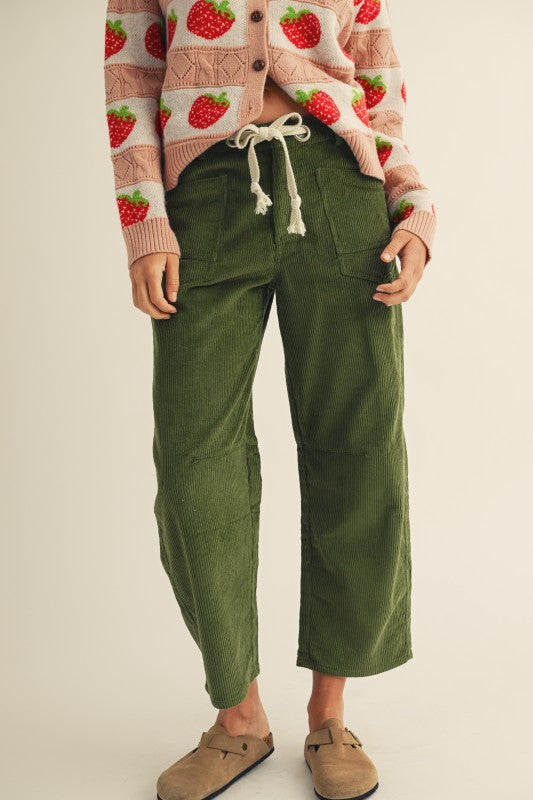 Person wearing a strawberry-patterned cardigan and green pants on a beige background