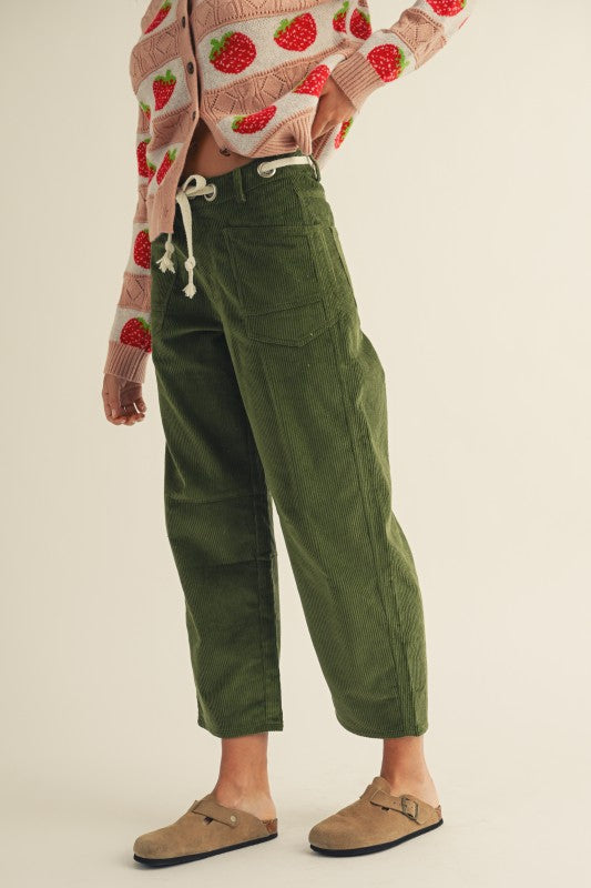 Person wearing green cargo pants with a strawberry-patterned sweater on a beige background
