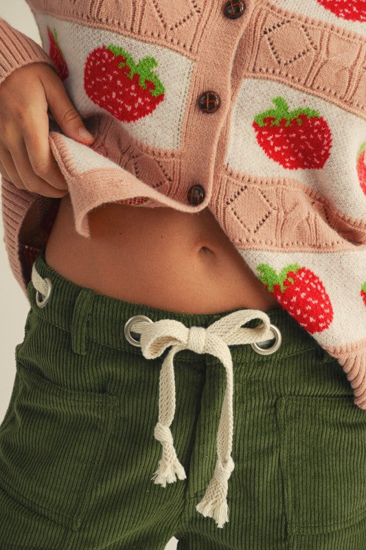 Person wearing a pink cardigan with strawberry pattern and green pants.