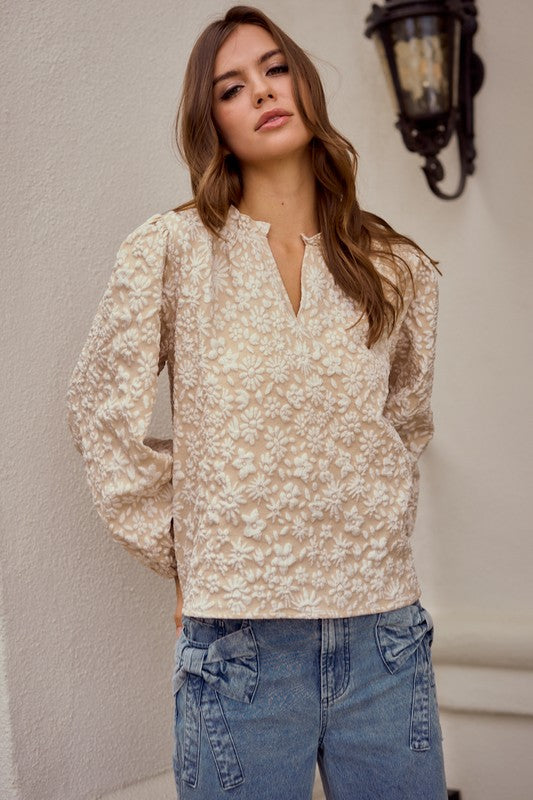 Woman wearing a floral blouse and jeans against a neutral wall.