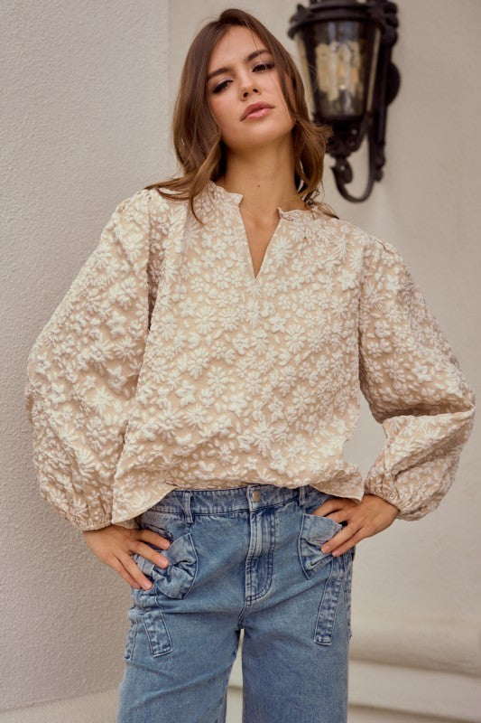 Woman wearing a floral blouse and jeans against a neutral wall.