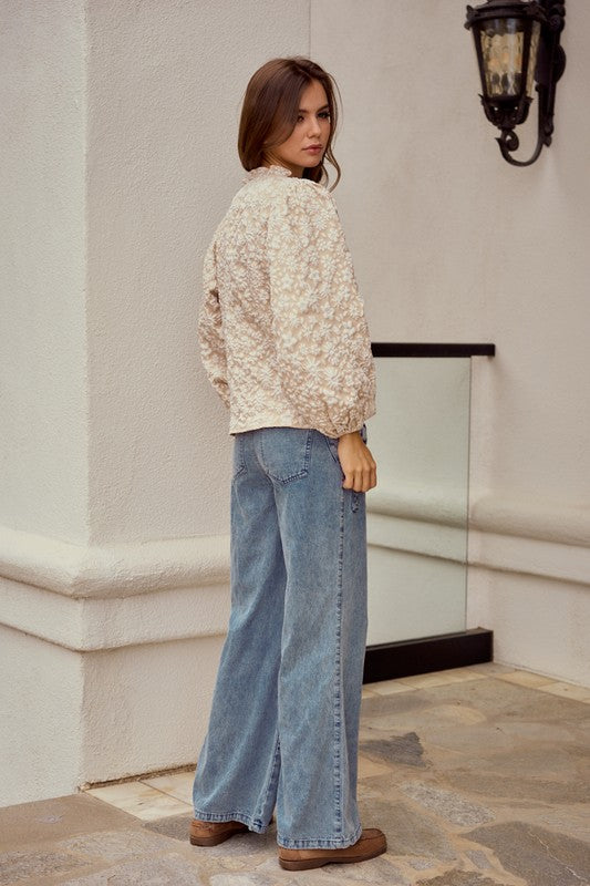 Woman wearing a floral blouse and blue jeans standing in an outdoor setting.