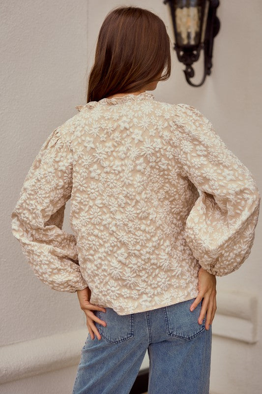 Woman wearing a floral blouse and blue jeans against a neutral background