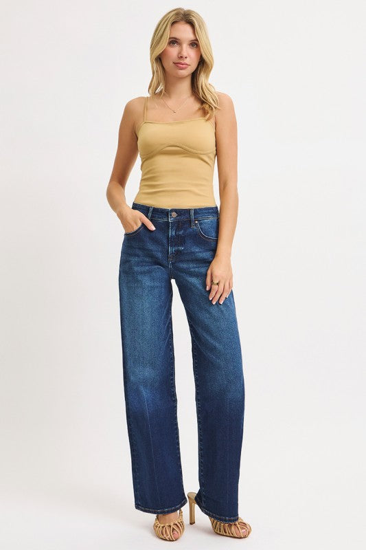 Woman wearing a beige tank top and blue jeans on a white background