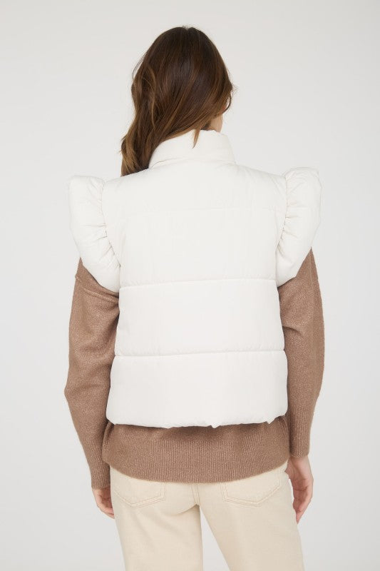 Person wearing a white puffer vest over a brown sweater on a white background