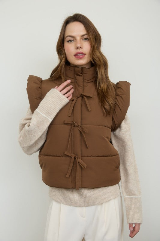 Woman wearing a brown puffer vest over a beige sweater on a white background