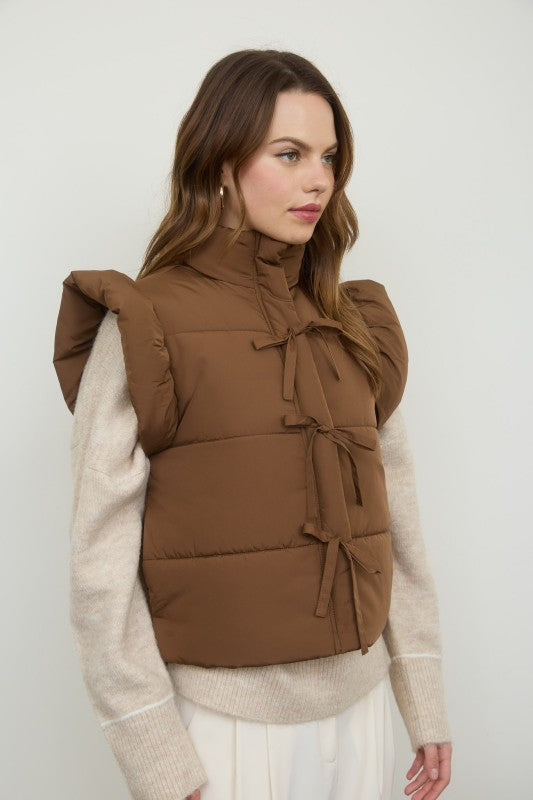 Woman wearing a brown puffer vest over a beige sweater against a white background