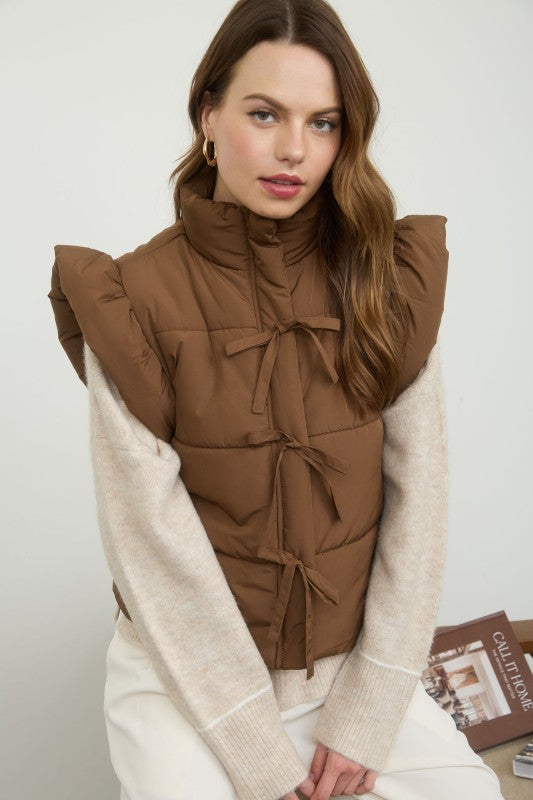 Woman wearing a brown puffer vest over a beige sweater with a plain background