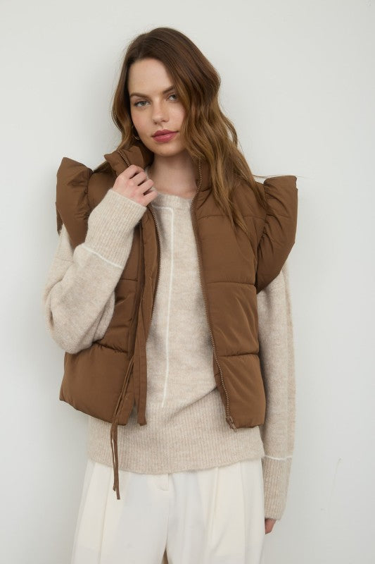 Woman wearing a brown puffer vest over a beige sweater against a white background