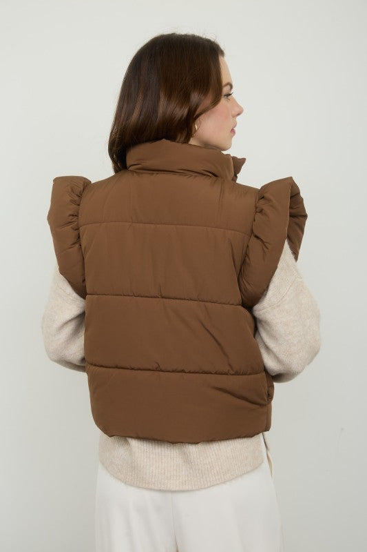 Woman wearing a brown puffer vest over a beige sweater against a white background