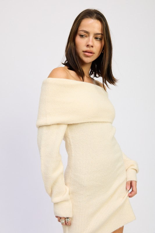Woman wearing a cream off-shoulder sweater dress against a plain background