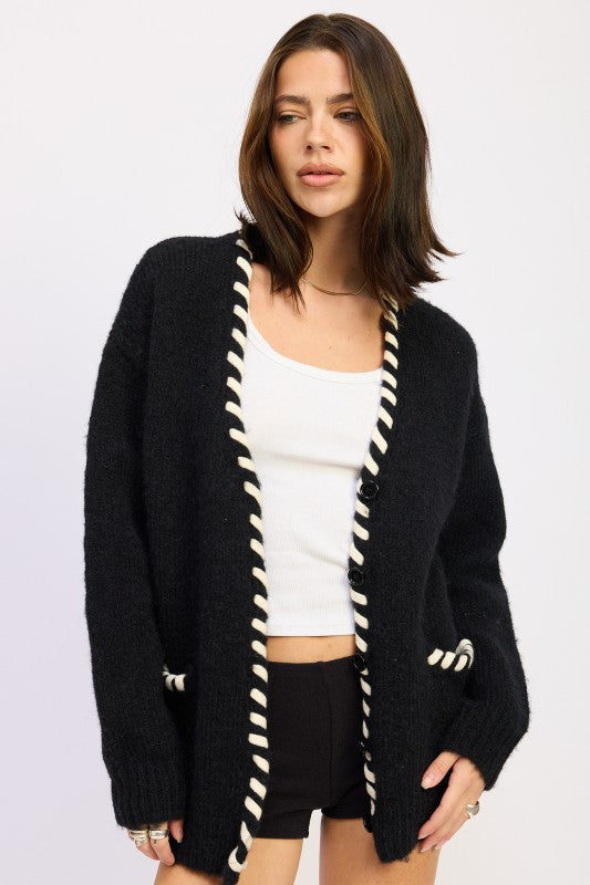 Woman wearing a black cardigan with white trim on a white background