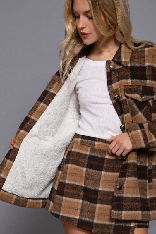 Woman wearing a plaid coat with a white shirt and skirt on a gray background